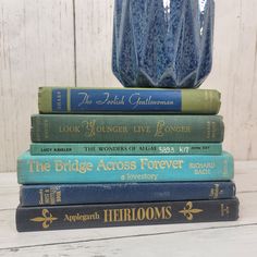 five books stacked on top of each other in front of a blue vase and white wooden wall