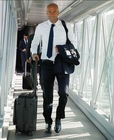 a man with a suit and tie pulling luggage down a walkway