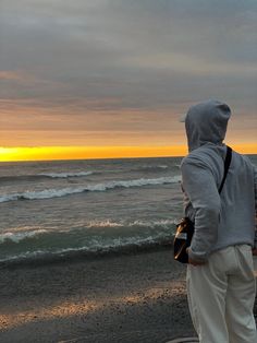 a man standing on the beach watching the sun go down over the ocean and waves