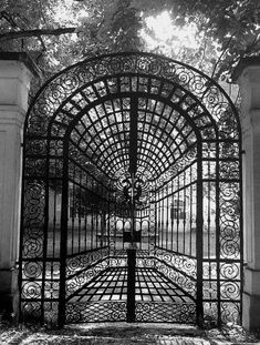 an iron gate in the middle of a park with pillars and arches on either side