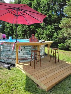 a woman sitting at a table with an umbrella over it in front of a pool