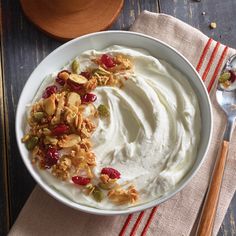 a bowl filled with yogurt and nuts on top of a table next to a spoon