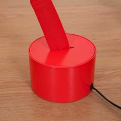 a red object is sitting on a wooden table with a black cord attached to it