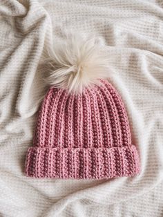 a pink knitted hat with a white pom - pom