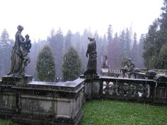 statues in the rain on top of a stone structure with trees in the back ground