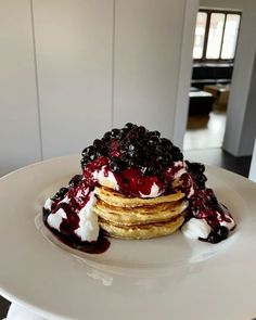 a stack of pancakes with blueberries and whipped cream on top sitting on a white plate