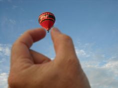 a hand holding a hot air balloon in the sky