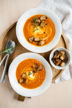 two white bowls filled with soup on top of a wooden tray next to silverware