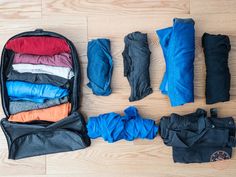 an open suitcase filled with clothes sitting on top of a wooden floor next to other items