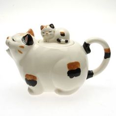 two cats sitting on top of a teapot shaped like a cat with its eyes closed