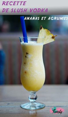 a glass filled with yellow liquid on top of a wooden table next to a blue straw