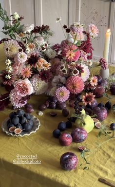 an arrangement of flowers and fruit on a table