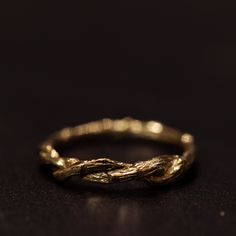 a gold wedding band with twisted branches on it's sides, sitting on a black surface