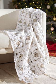 a white crocheted blanket sitting on top of a couch next to a christmas tree