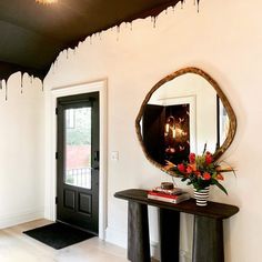 a foyer with a mirror, vase and flowers on the table in front of it