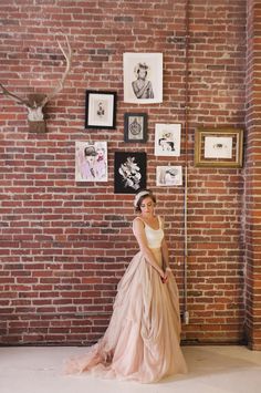 a woman standing in front of a brick wall with pictures on the wall behind her