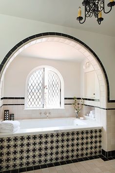 a bathroom with an arched window and black and white tiles on the walls, along with a large bathtub