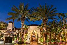 palm trees line the front entrance to a house at night with bright lights on it