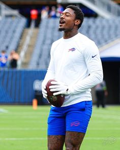 a man holding a football in his right hand and wearing blue shorts on the field