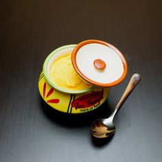 two bowls with spoons sitting next to each other on a black counter top, one has an orange and white lid