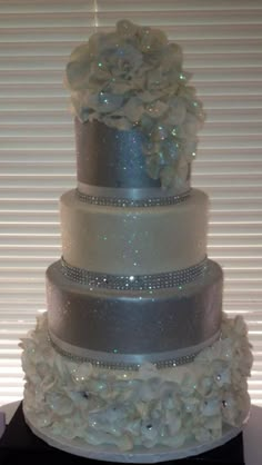 a three tiered wedding cake with white flowers on the top and silver ribbon around the bottom