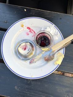 a white plate topped with two small jars filled with jelly and jam next to a spoon