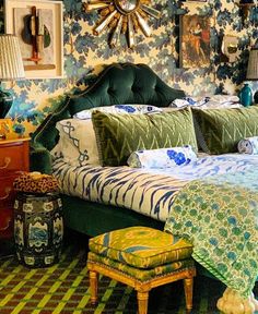 a bed with green headboard and foot stool in a room filled with pictures on the wall