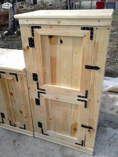 an unfinished wooden cabinet with black handles and latches on the doors is sitting outside