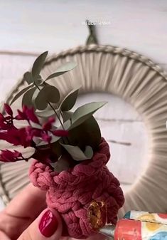 a hand holding a crochet ring with flowers in it and a bottle of nail polish next to it