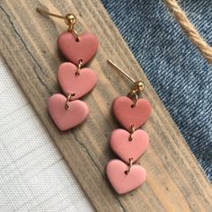 pink heart shaped earrings hanging from hooks on a wooden board next to a pair of jeans