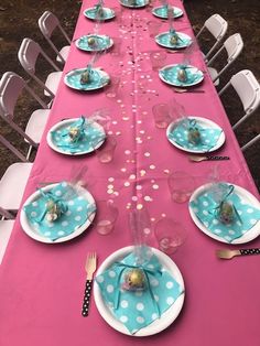 the table is set with pink and blue plates, silverware, and confetti