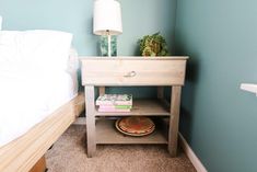 a nightstand with books on it next to a white bed and blue walls in a bedroom