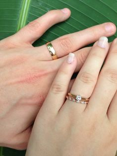 two people holding hands with wedding rings on top of each other and green leaf in the background