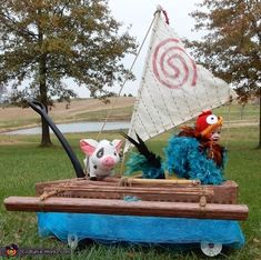 two stuffed animals are sitting on a toy boat in the grass with a sailboat behind them