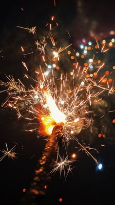 a person holding a sparkler in their hand with fireworks coming out of it at night