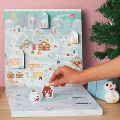 a person is holding a paper cutout in front of a box with houses and animals on it