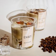 two glasses filled with ice and coffee on top of a white table next to some beans