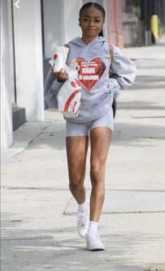 a woman in grey sweatshirt and shorts walking down the street