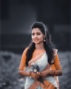 a woman in an orange and white sari with flowers on her lap, smiling at the camera