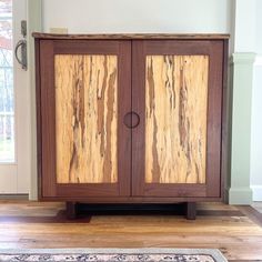 a wooden cabinet sitting on top of a hard wood floor next to a rug and window