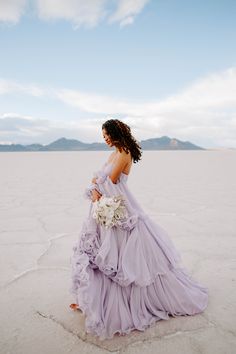 a woman in a purple dress is standing on the beach with her back to the camera