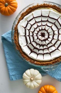 there is a pie with white frosting and chocolate decorations on the top, surrounded by mini pumpkins