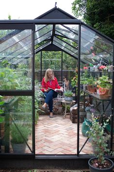 a woman is sitting in a greenhouse with potted plants on the floor and inside