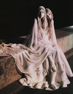 two women dressed in white are sitting on a ledge at night with their heads turned to the side