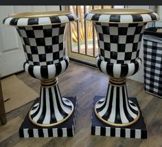 two black and white checkered vases sitting on stands in front of a window