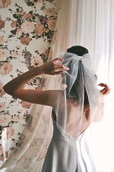 a woman wearing a veil and dress in front of a floral wallpapered room