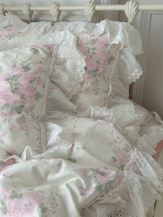 an unmade bed with pink flowers and white ruffled bedspread on it