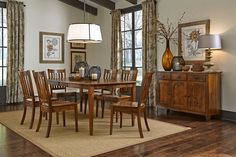 a dinning room table with chairs and lamps on the sideboard in front of windows