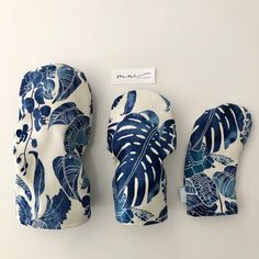 three oven mitts with blue and white leaves on them, next to a tag