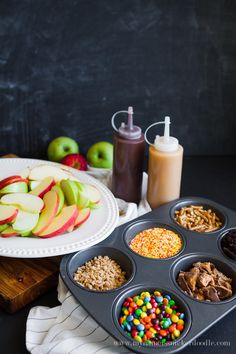 a muffin tin filled with lots of fruit and cereals next to an apple